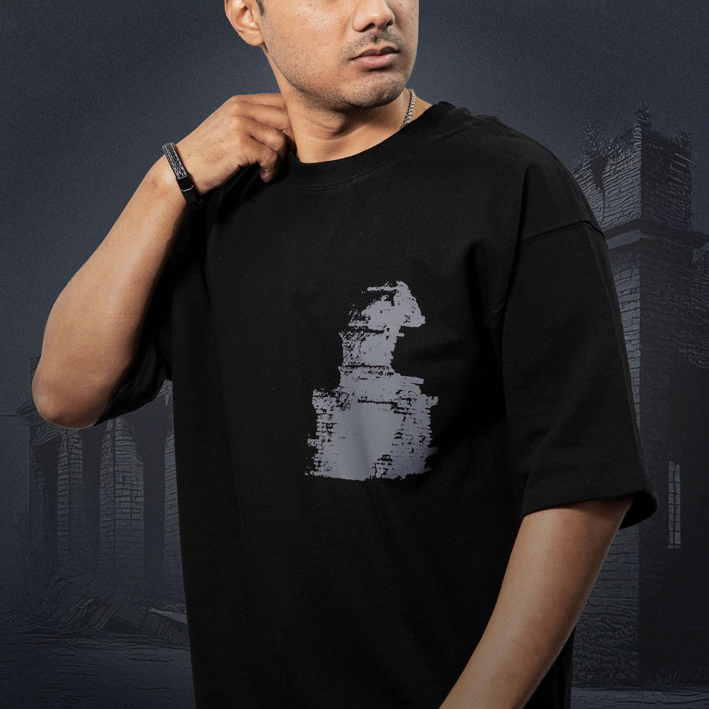 Man wearing Dhanushkodi black oversized t-shirt with a graphic design, standing against a dark background.