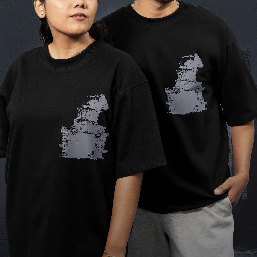 Two people wearing Dhanushkodi black oversized t-shirts with a graphic design on a dark background