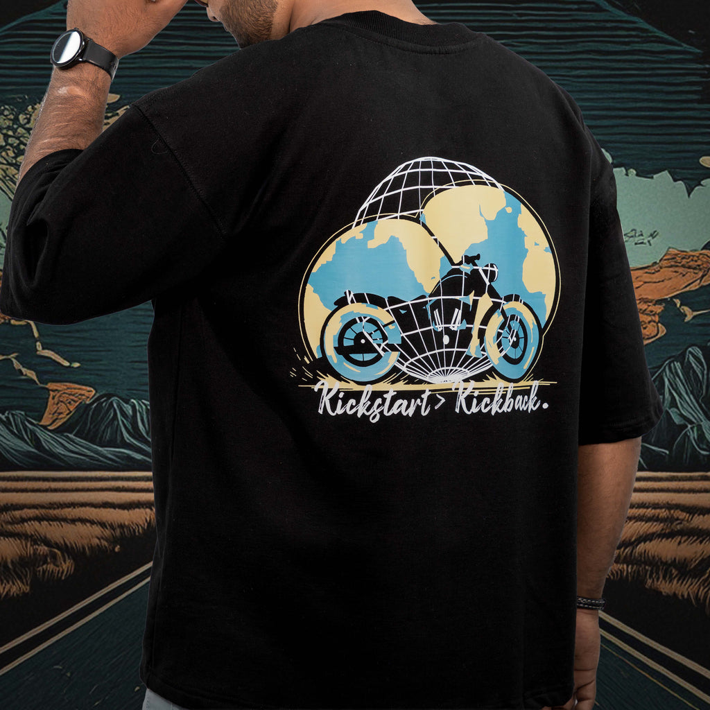 Person wearing a kickstart black oversized t-shirt with a graphic design on the back, standing in front of a colorful mural.