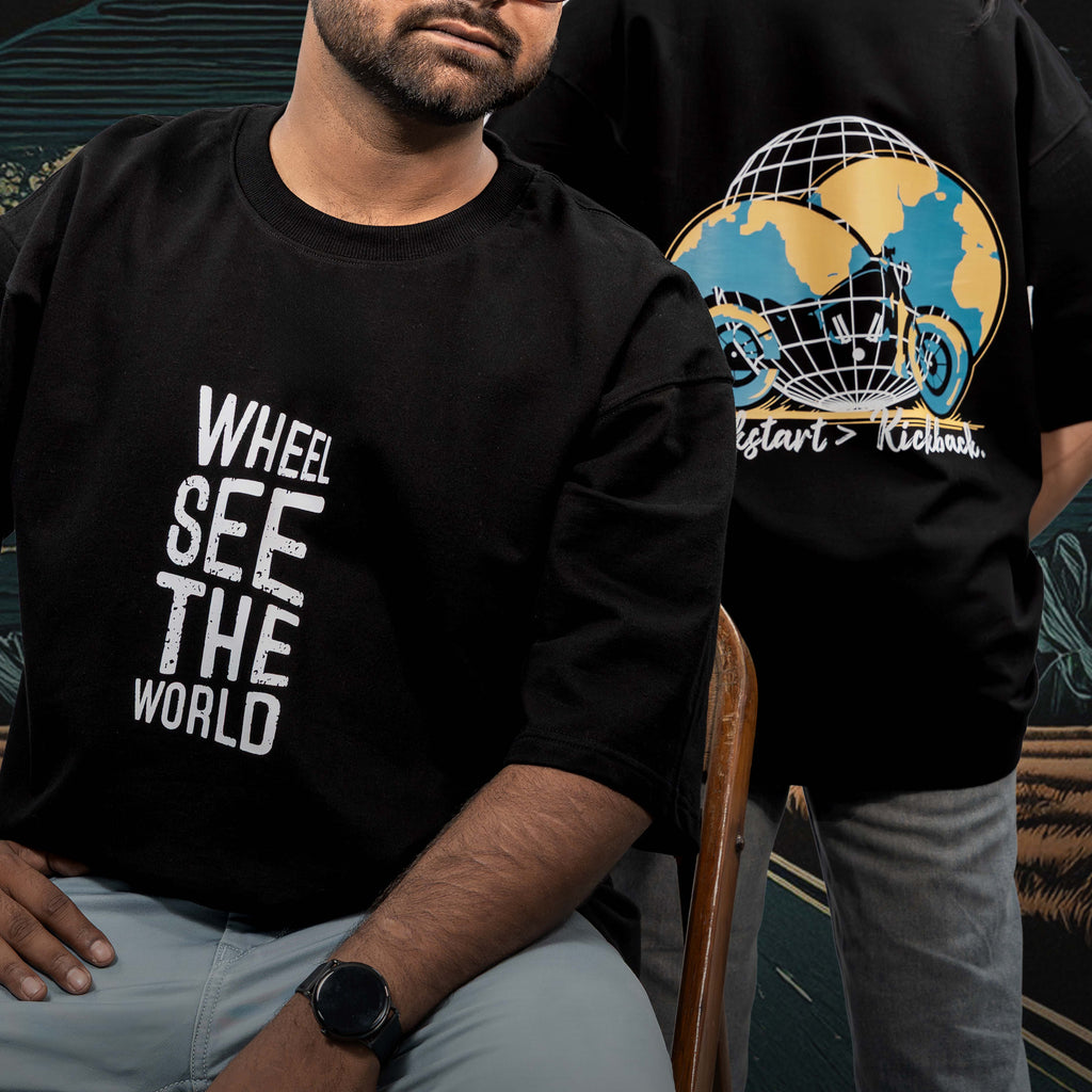 Two people wearing kickstart black oversized t-shirts with different designs worn by a person sitting on a chair.
