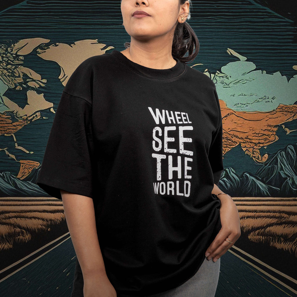 Person wearing a kickstart black oversized t-shirt with 'Whee! See The World' text in front of a world map.