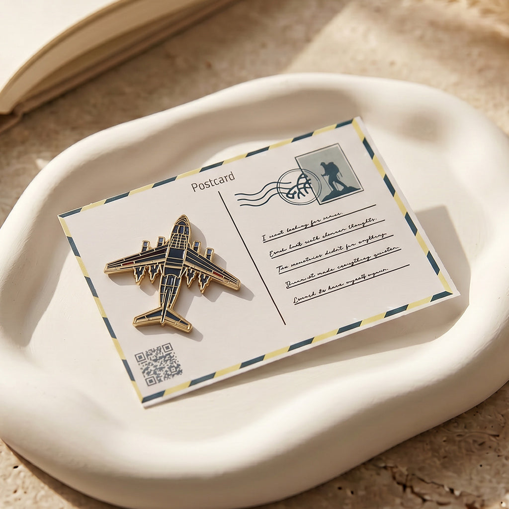 Gold airplane pin on a postcard with a QR code on a beige surface
