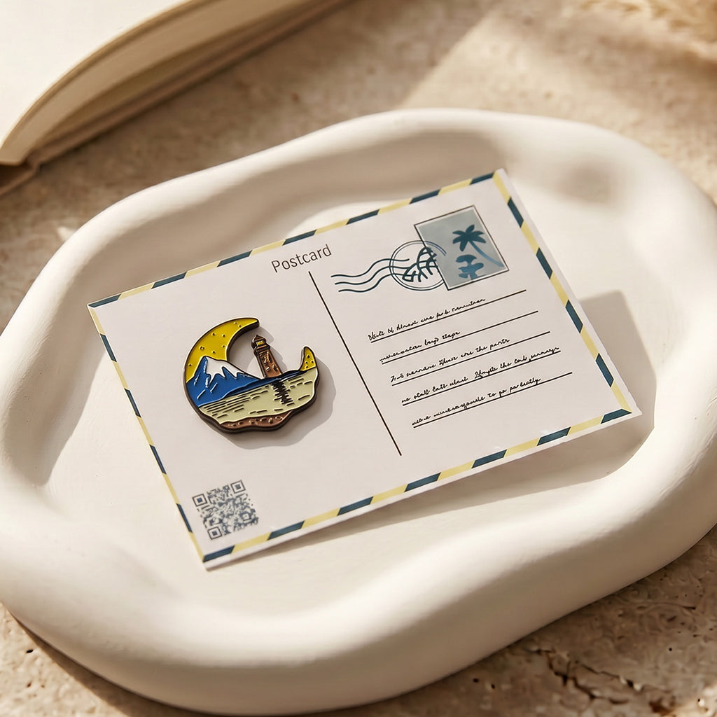 Pin with mountain and lighthouse design on a postcard with a stamp on a beige surface