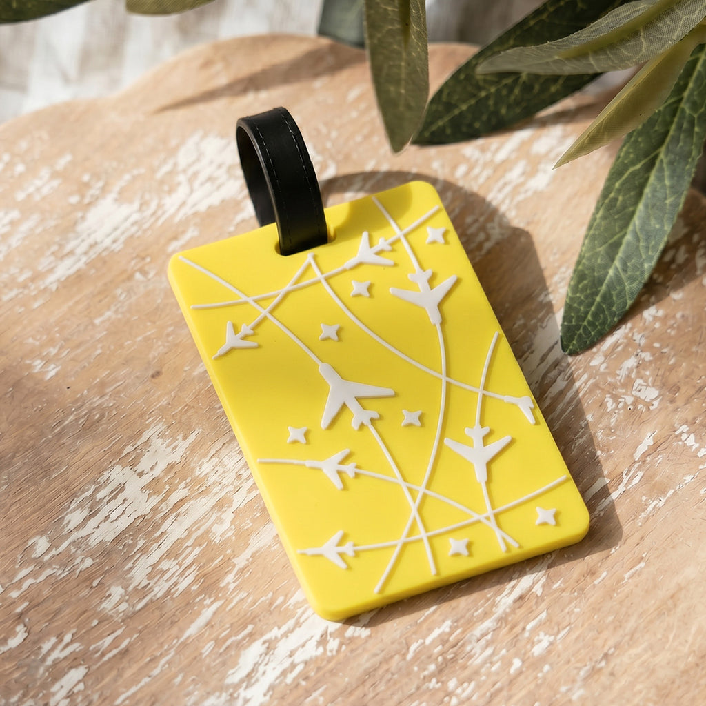 Yellow luggage tag with airplane and star patterns on a wooden surface with leaves.