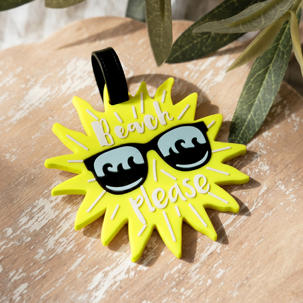 Yellow sun-shaped pendant with sunglasses and 'Beach Please' text on a wooden surface.
