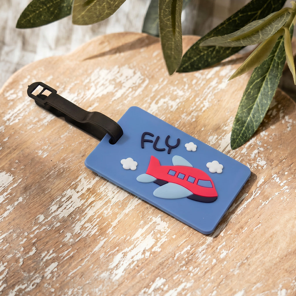 Luggage tag with airplane design and 'FLY' text on a wooden surface with leaves in the background