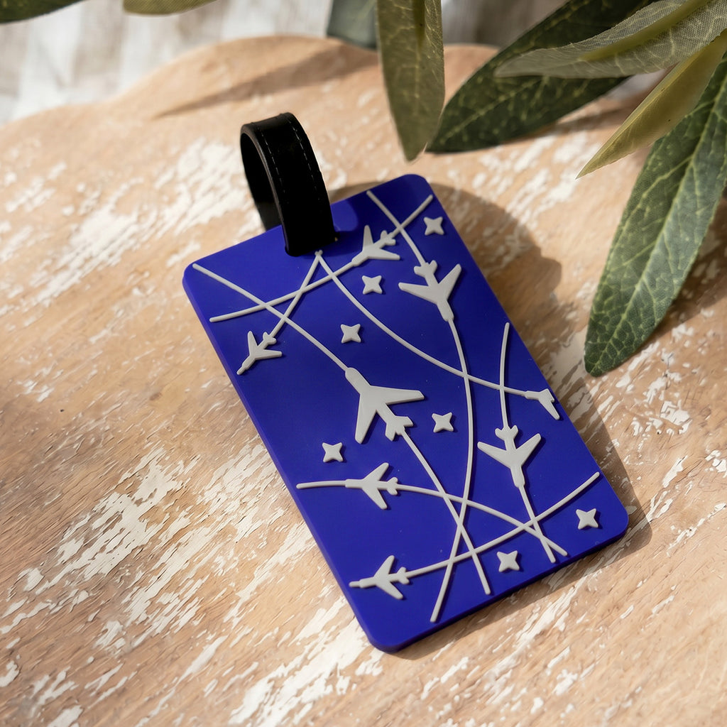 Blue luggage tag with white airplane and star designs on a wooden surface with leaves in the background