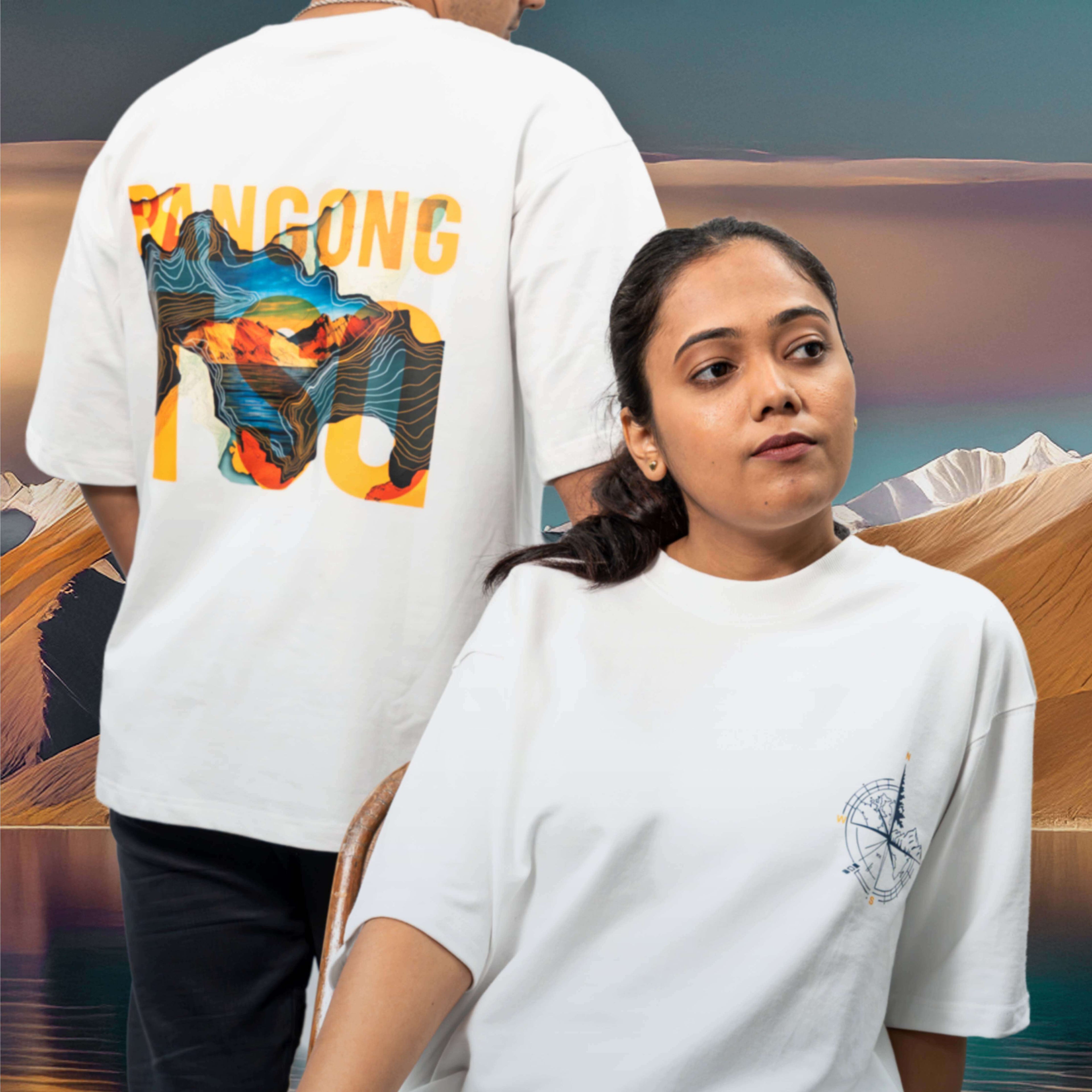 Two people wearing Pangong Tso white oversized t-shirts with colourful designs in a desert setting