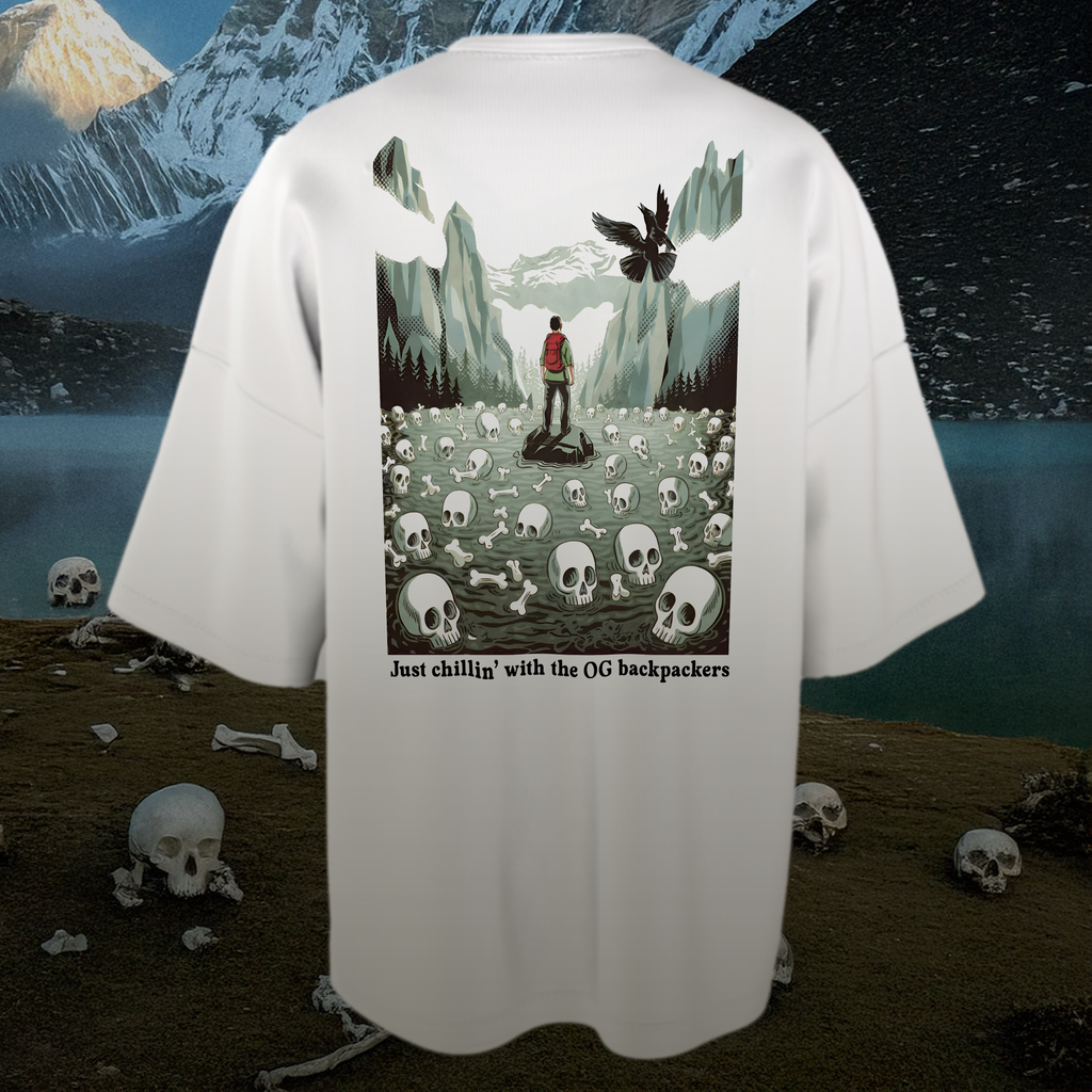 White oversized t-shirt with a graphic design of a person standing among skulls and bones with mountains in the background.