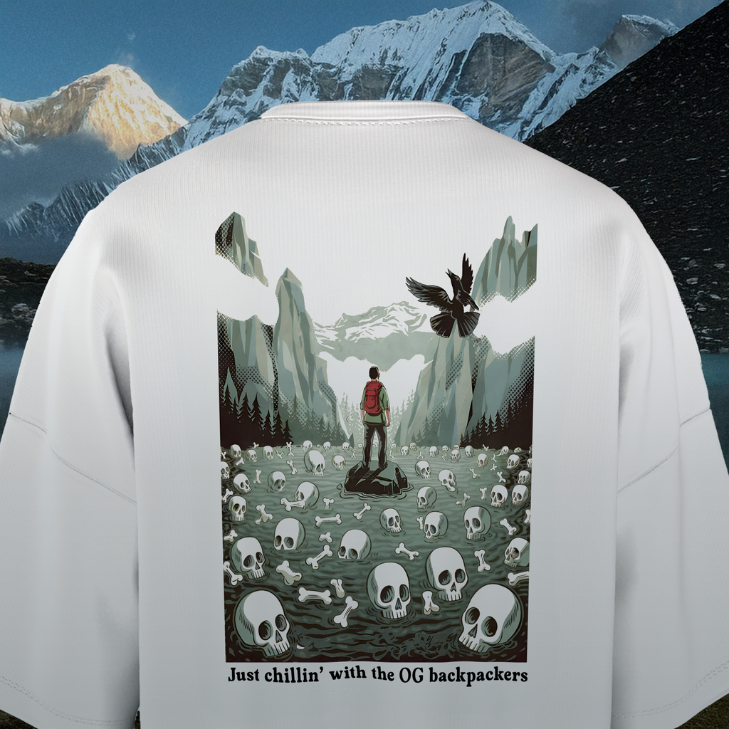 Back of a white oversized t-shirt with a graphic design of a person with a backpack in a mountainous landscape with skulls and bones.