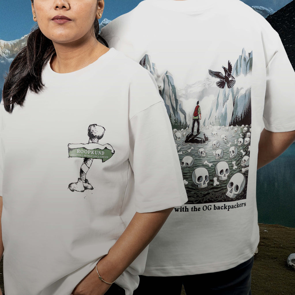 Two people wearing Roopkund white oversized t-shirts with unique designs, one featuring a skeleton and sign, the other with a mountain and skull design.