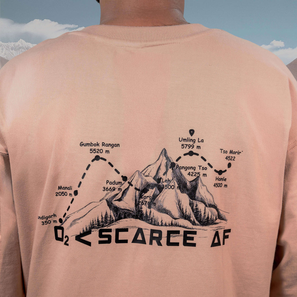Person wearing an Umling La Beige Oversized t-shirt with a mountain graphic and text on the back, against a mountainous landscape.