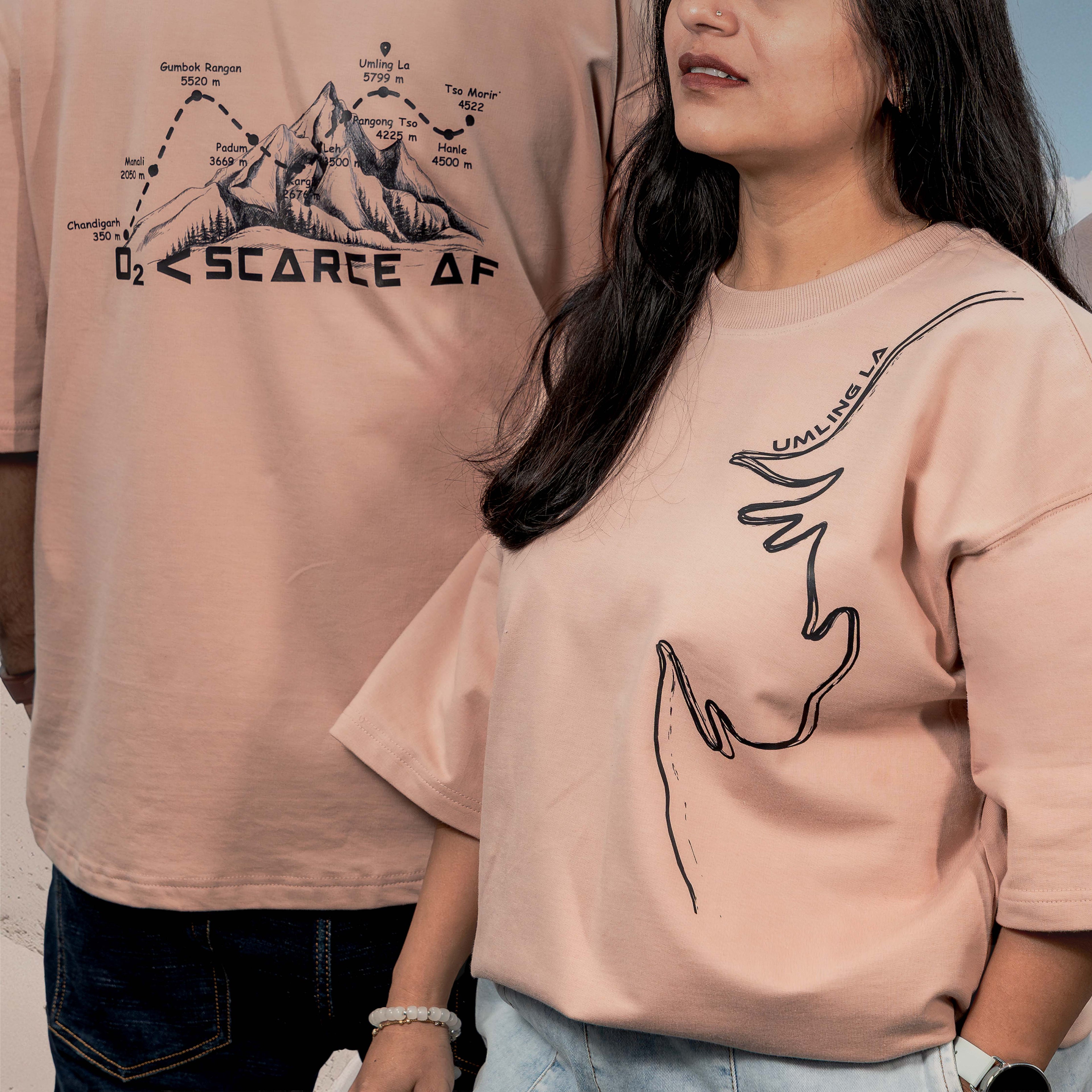 Two people wearing Umling La Beige Oversized t-shirts with black graphics and text.