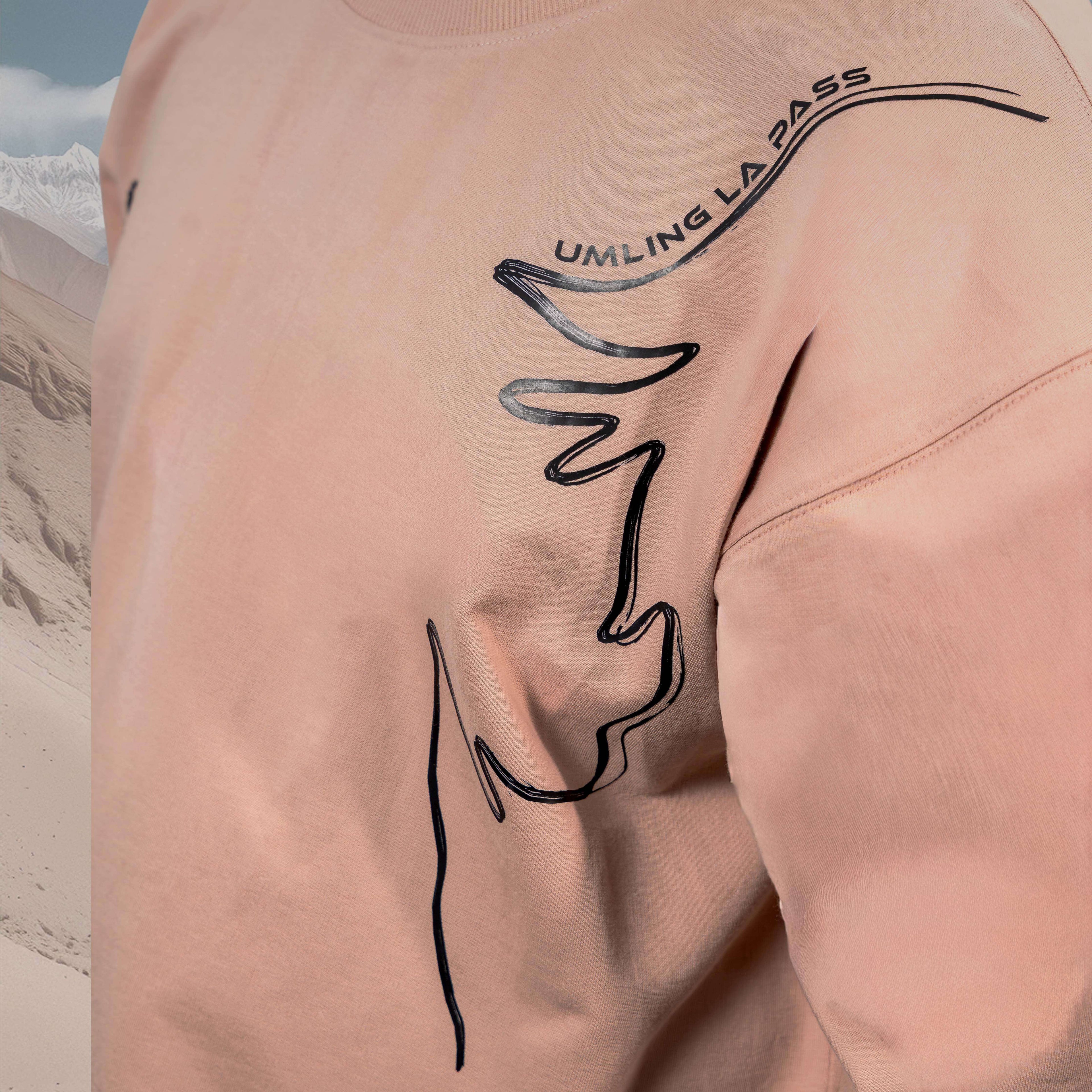 Person wearing an Umling La Beige oversized t-shirt with black line art design showing umling la route and text on a mountainous background