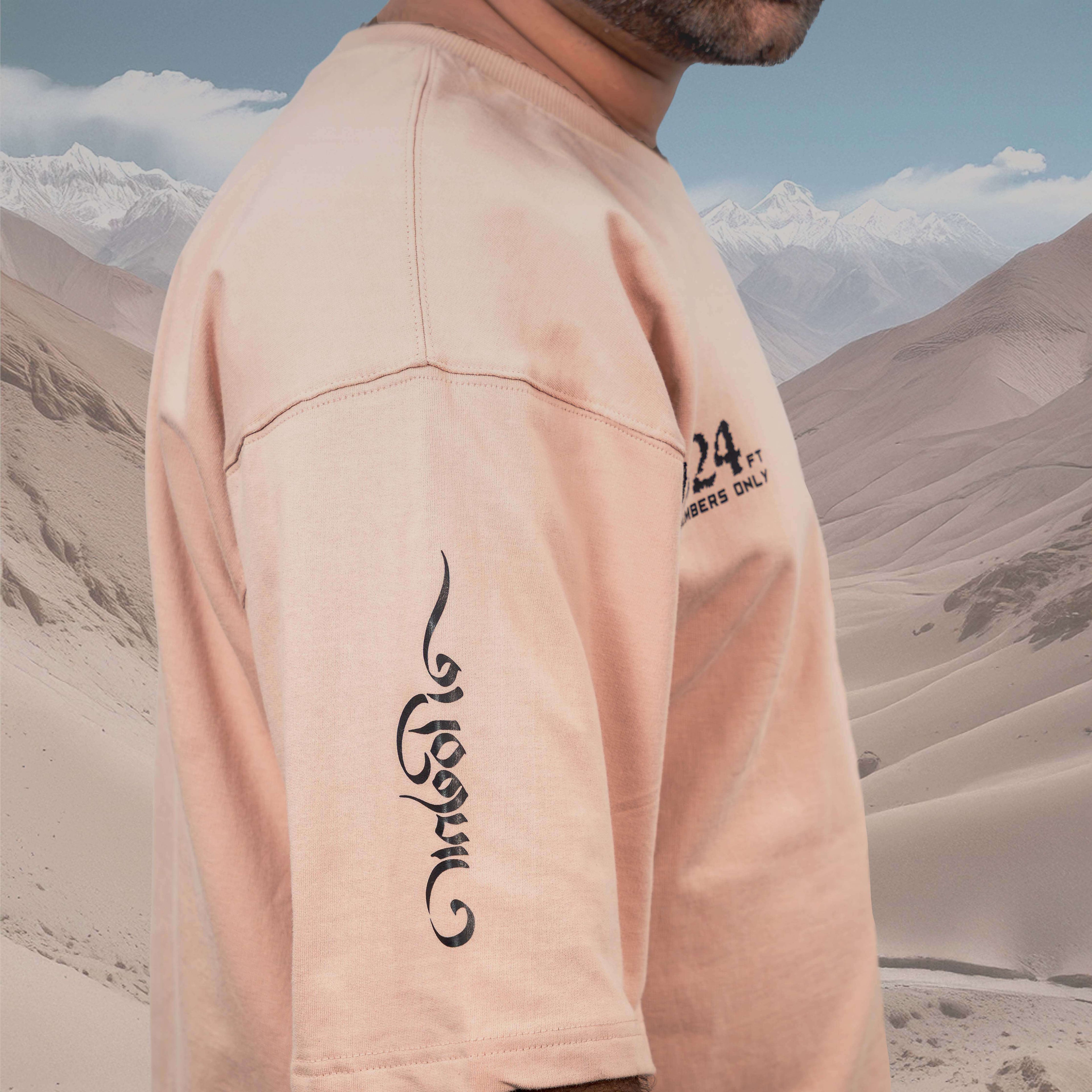 Person wearing an Umling La beige oversized t-shirt with long-sleeve and text written "BREATHE" in TIBET language in a desert landscape