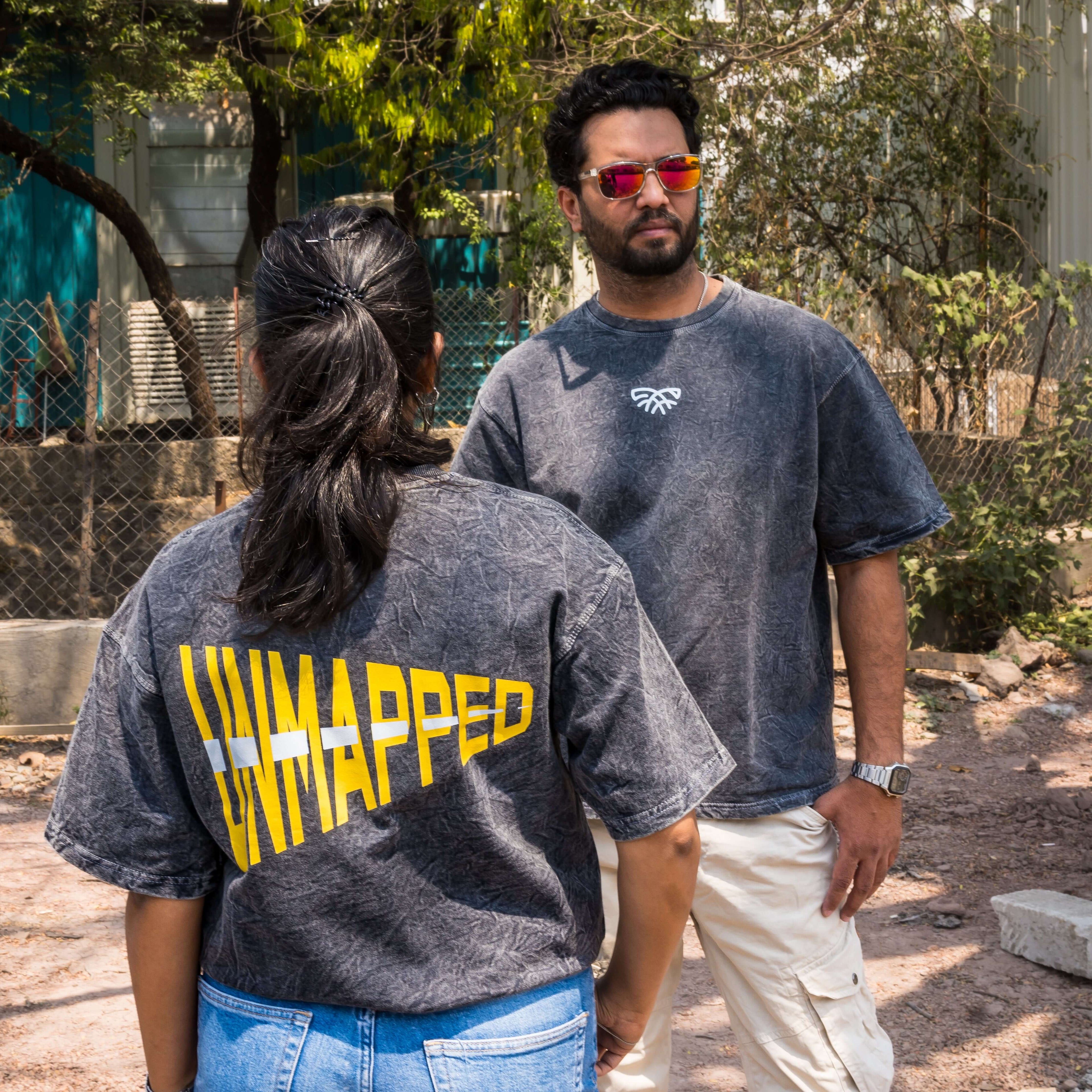 Two people wearing acid wash t-shirts with 'UNMAPPED' text outdoors.