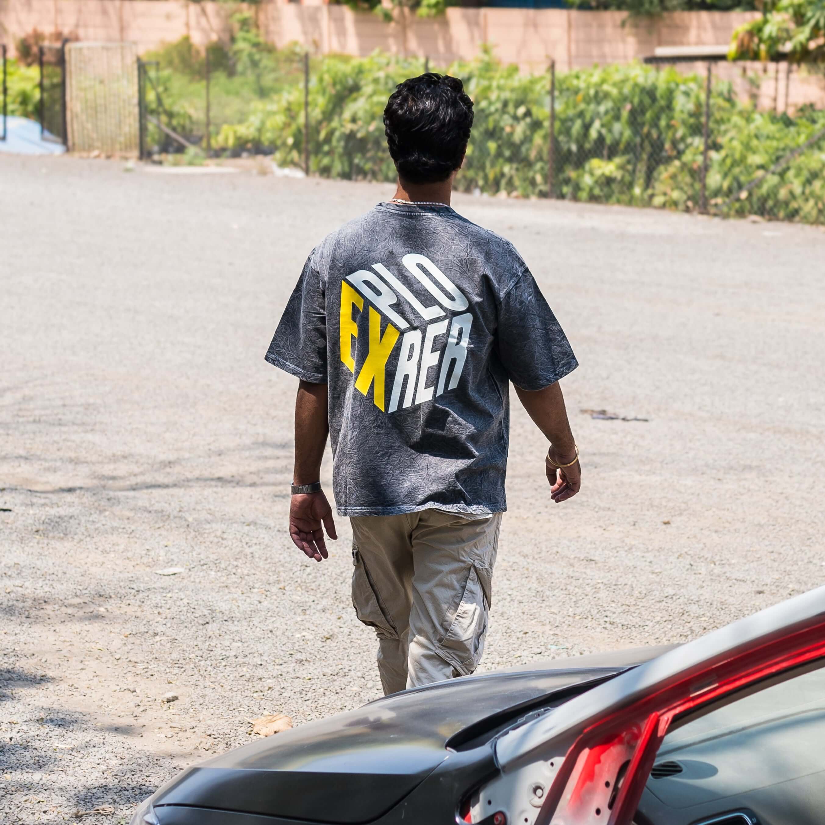 Person walking away from a car wearing acid wash t-shirt  in an outdoor setting