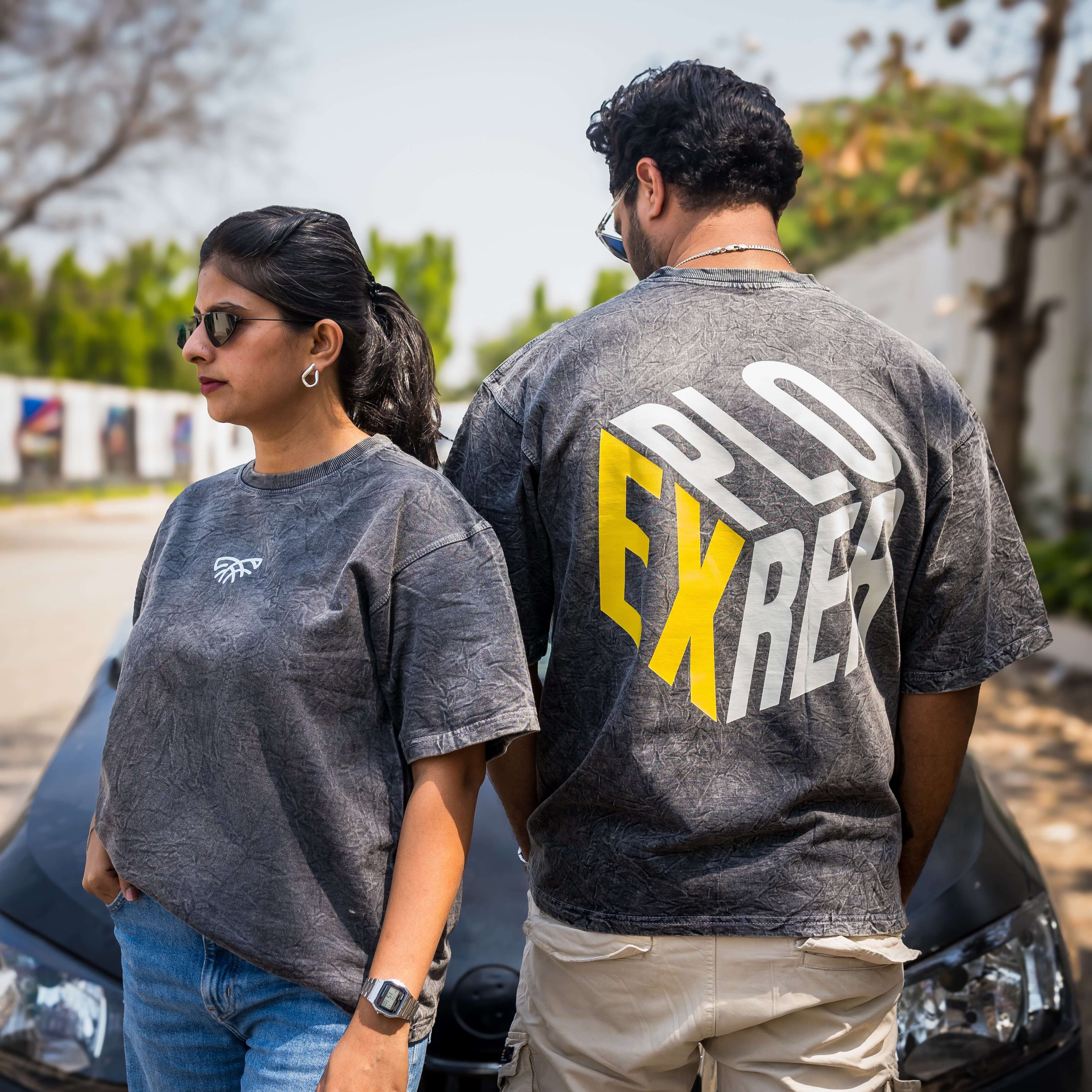 Two people wearing acid wash t-shirts, one with a logo on the front and the other with 'EXPLORER' on the back.