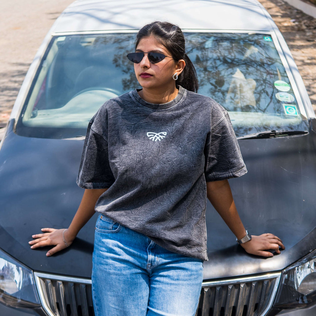 Woman standing in front of a car wearing sunglasses and acid wash t-shirt with a logo.