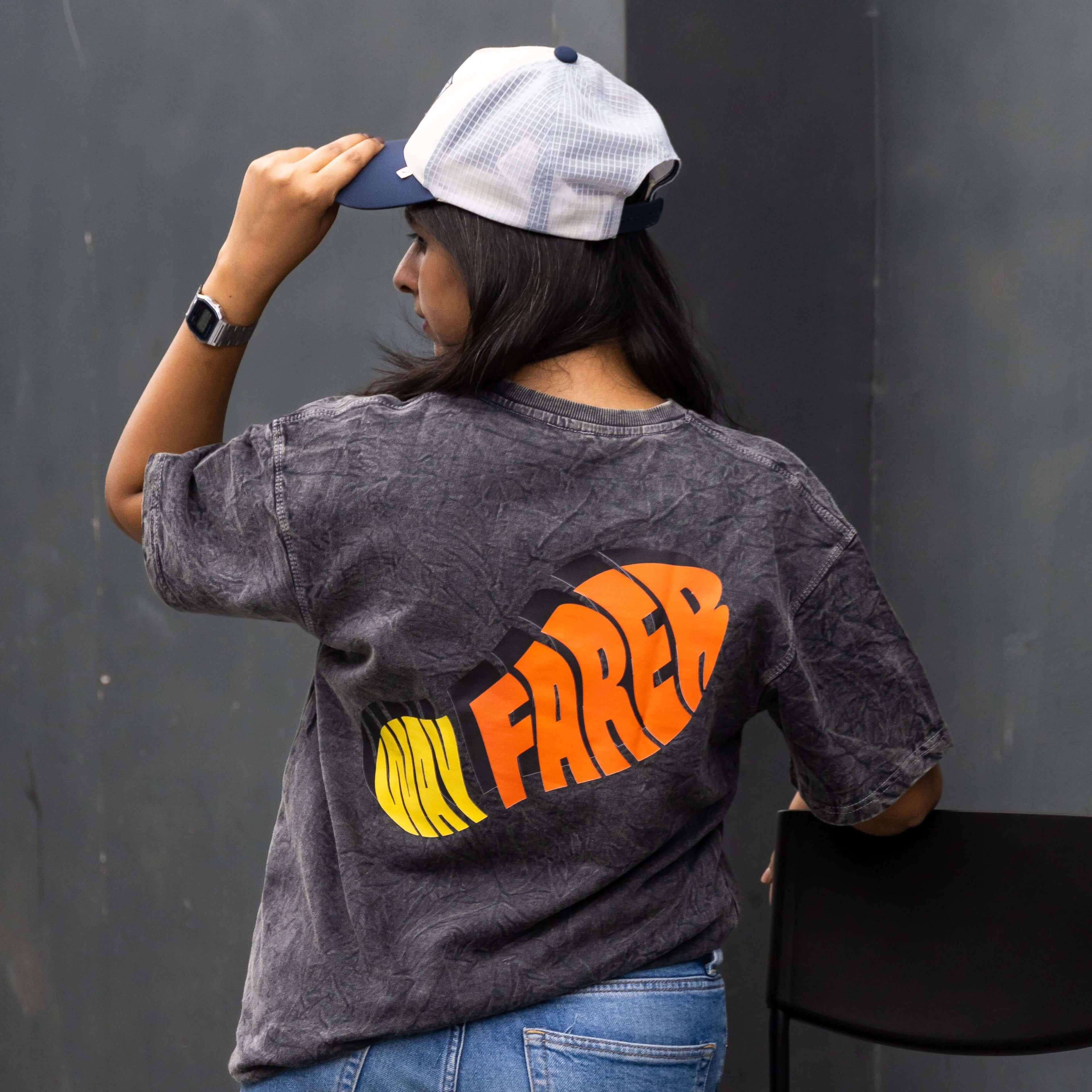 Person wearing acid wash t-shirt with wayfarer text, sitting on a black chair against a dark background.