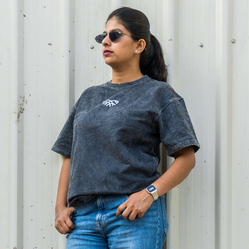 Woman wearing acid wash t-shirt and blue jeans standing against a corrugated metal wall.