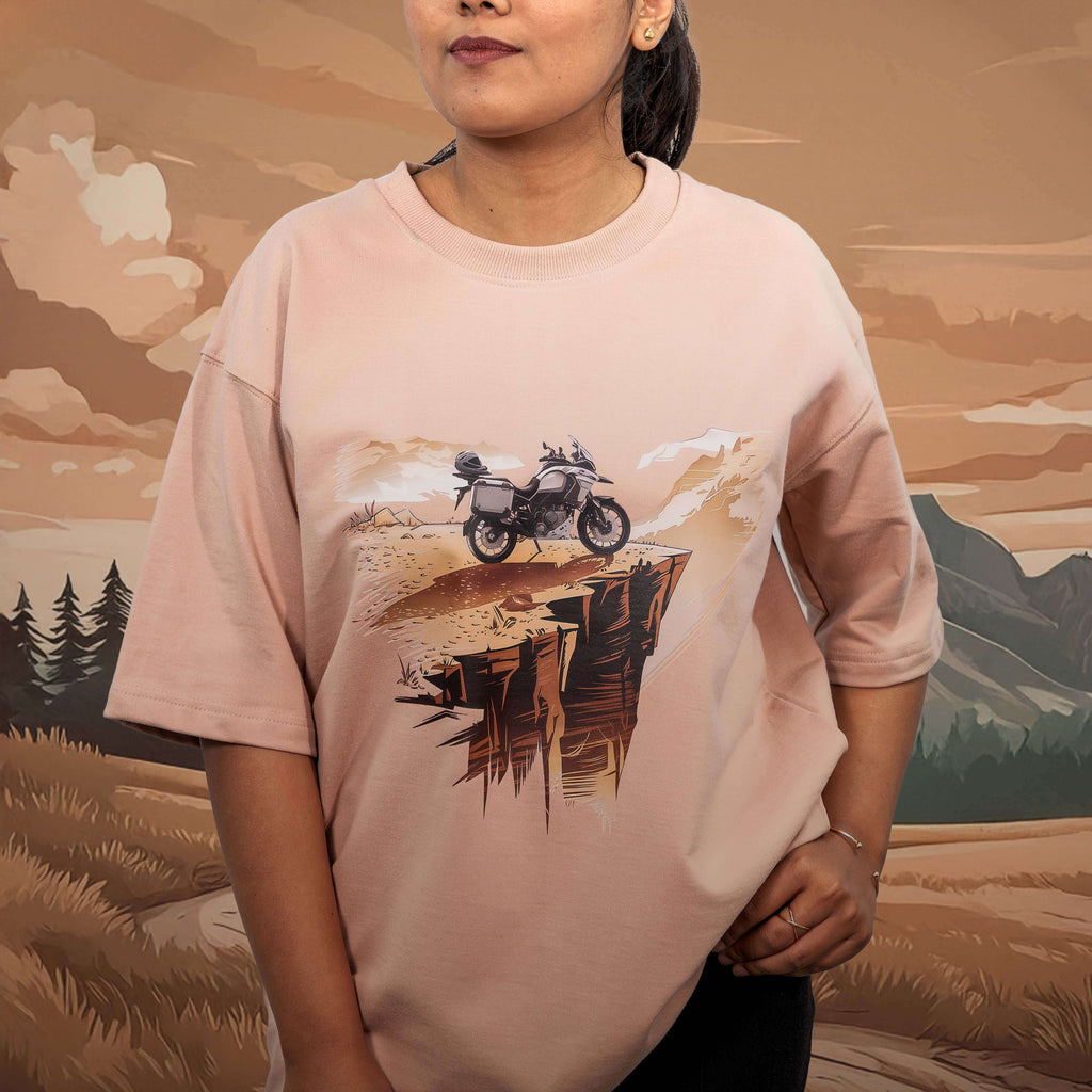 Person wearing a lost the wifi beige oversized t-shirt with a motorcycle graphic against a scenic background
