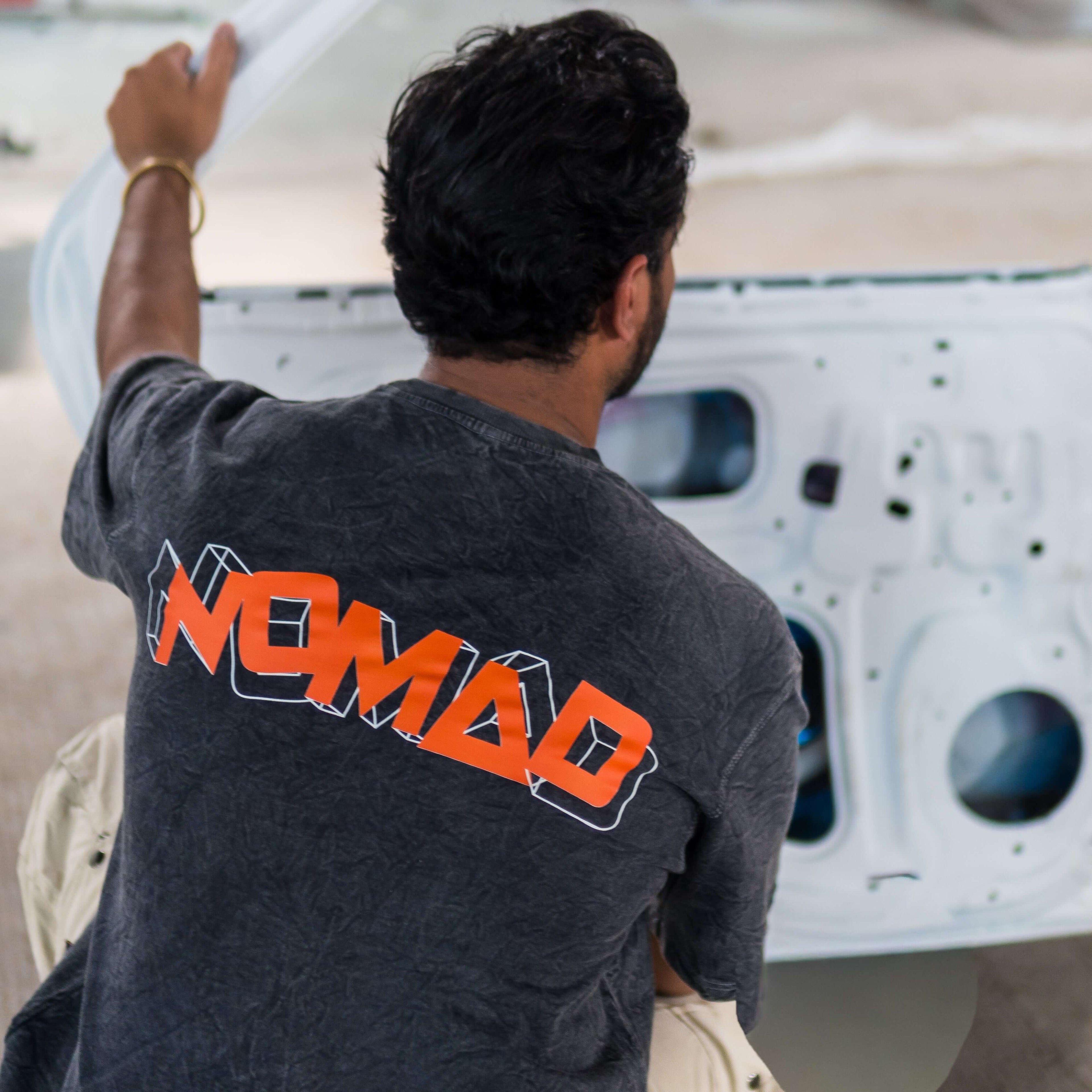 Person wearing acid wash t-shirt with 'Nomad' print working on a vehicle.
