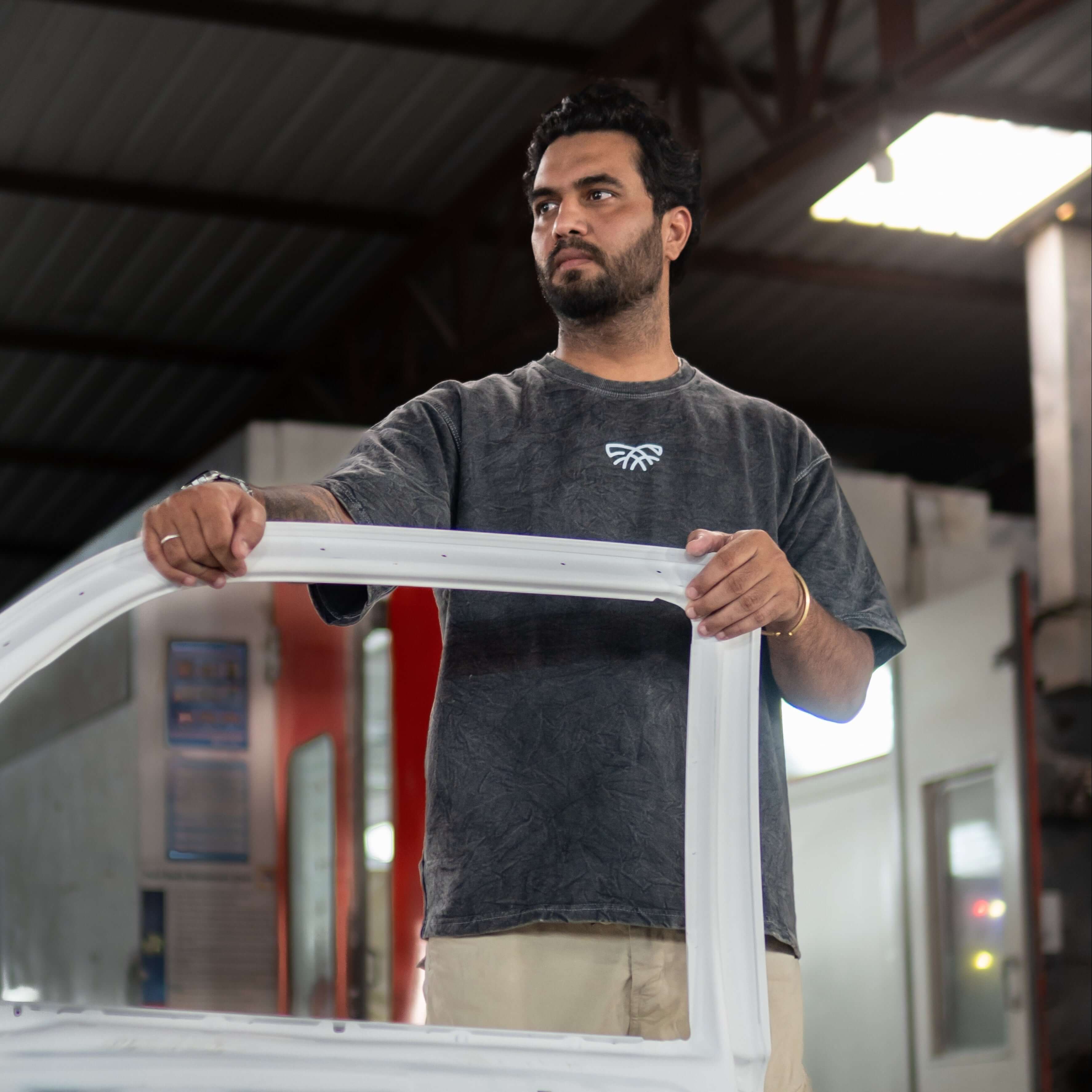 Man wearing acid wash t-shirt and holding a car door frame in a workshop setting