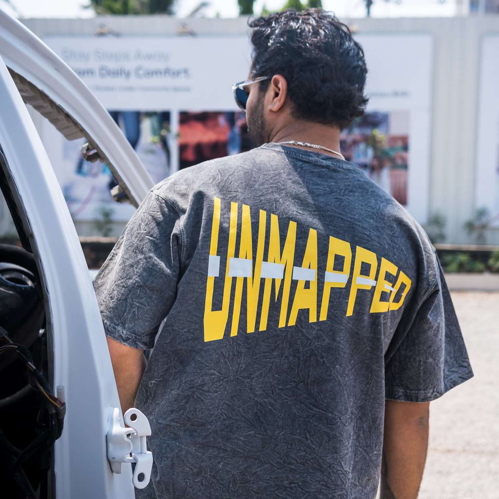 Person wearing an oversized t-shirt acid wash with 'UNMAPPED' printed on the back, standing next to a vehicle.