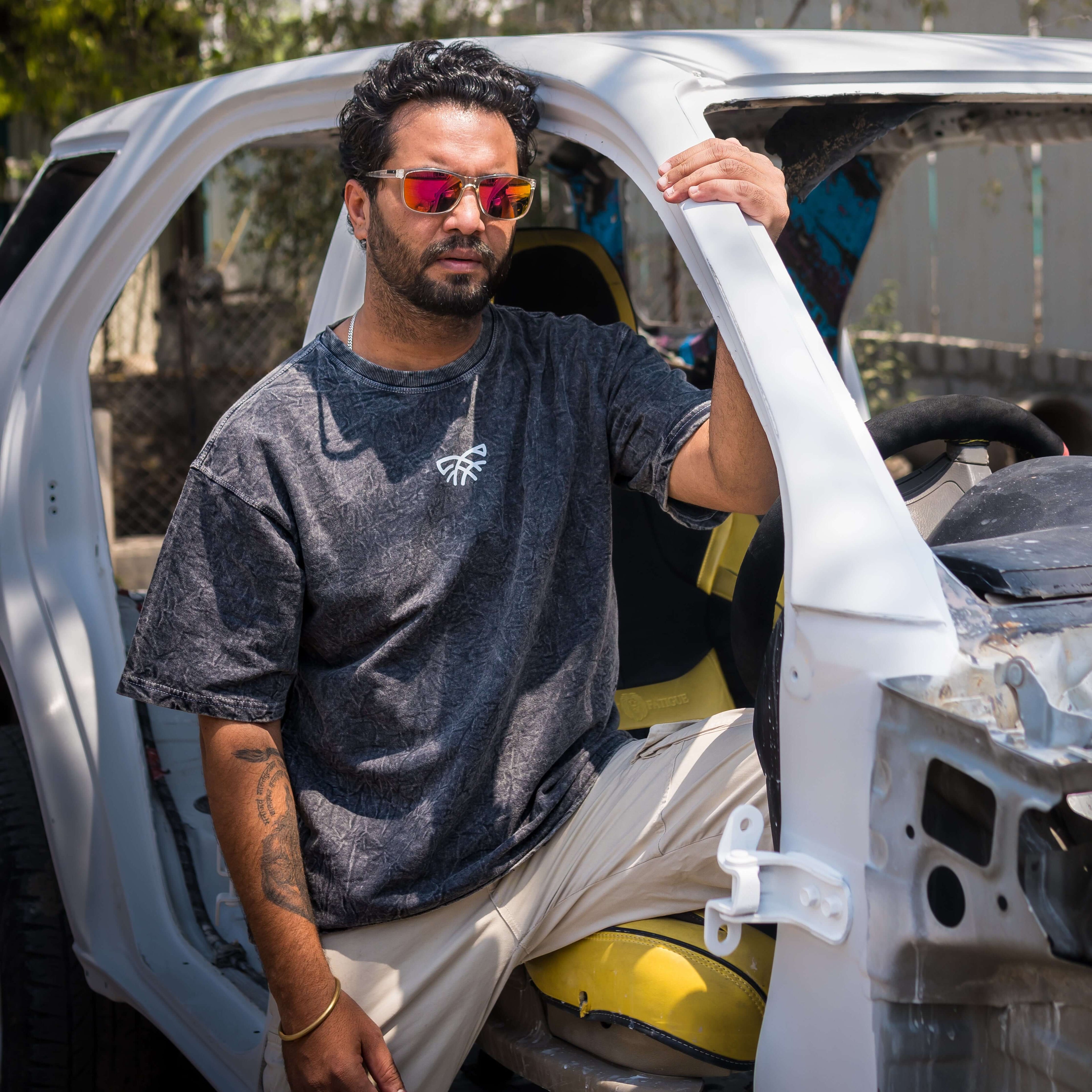 Man with sunglasses wearing acid wash oversized t-shirt sitting inside a white vehicle with an open door.