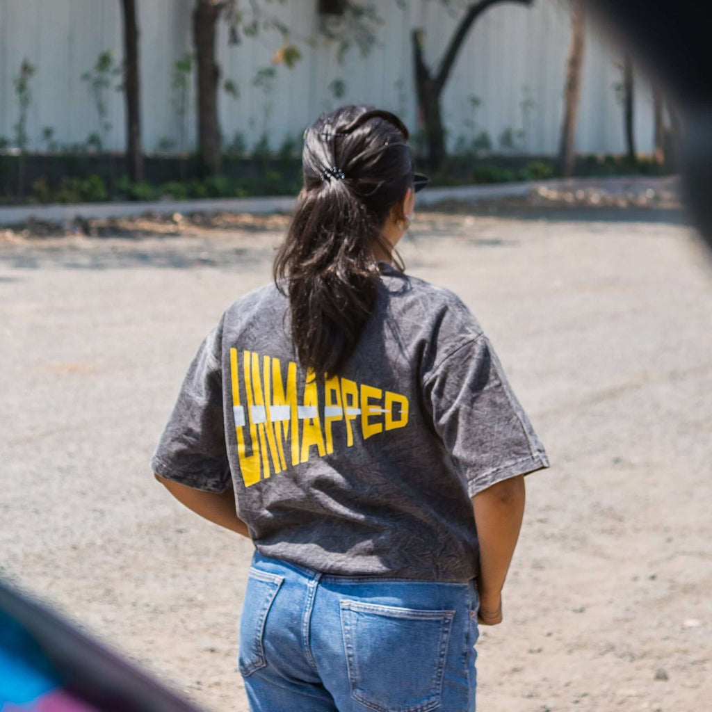Women wearing an acid wash oversized t-shirt with 'UNMAPPED' printed on the back, standing in a park-like setting.