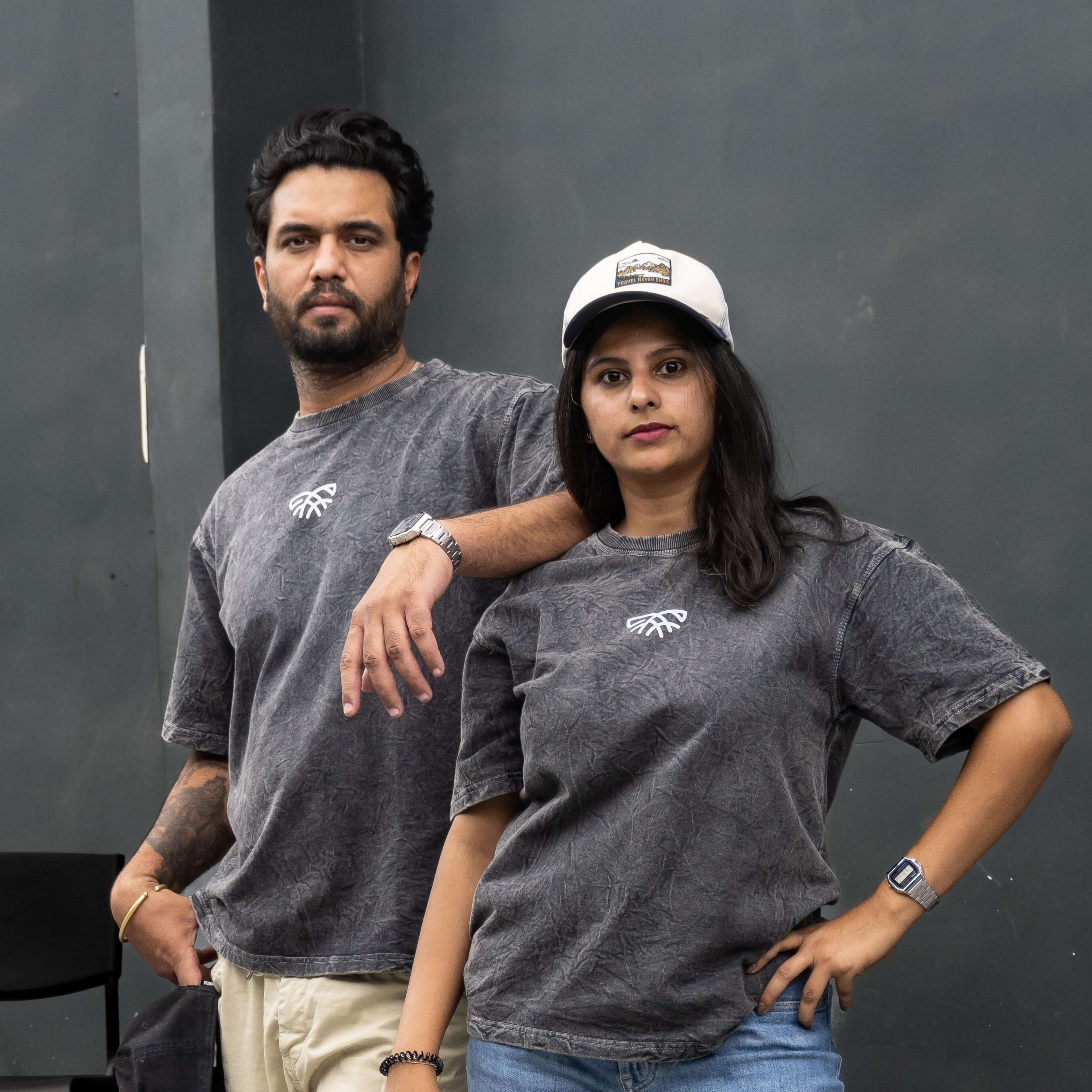 Two people wearing acid wash t-shirts with a logo against a black background.